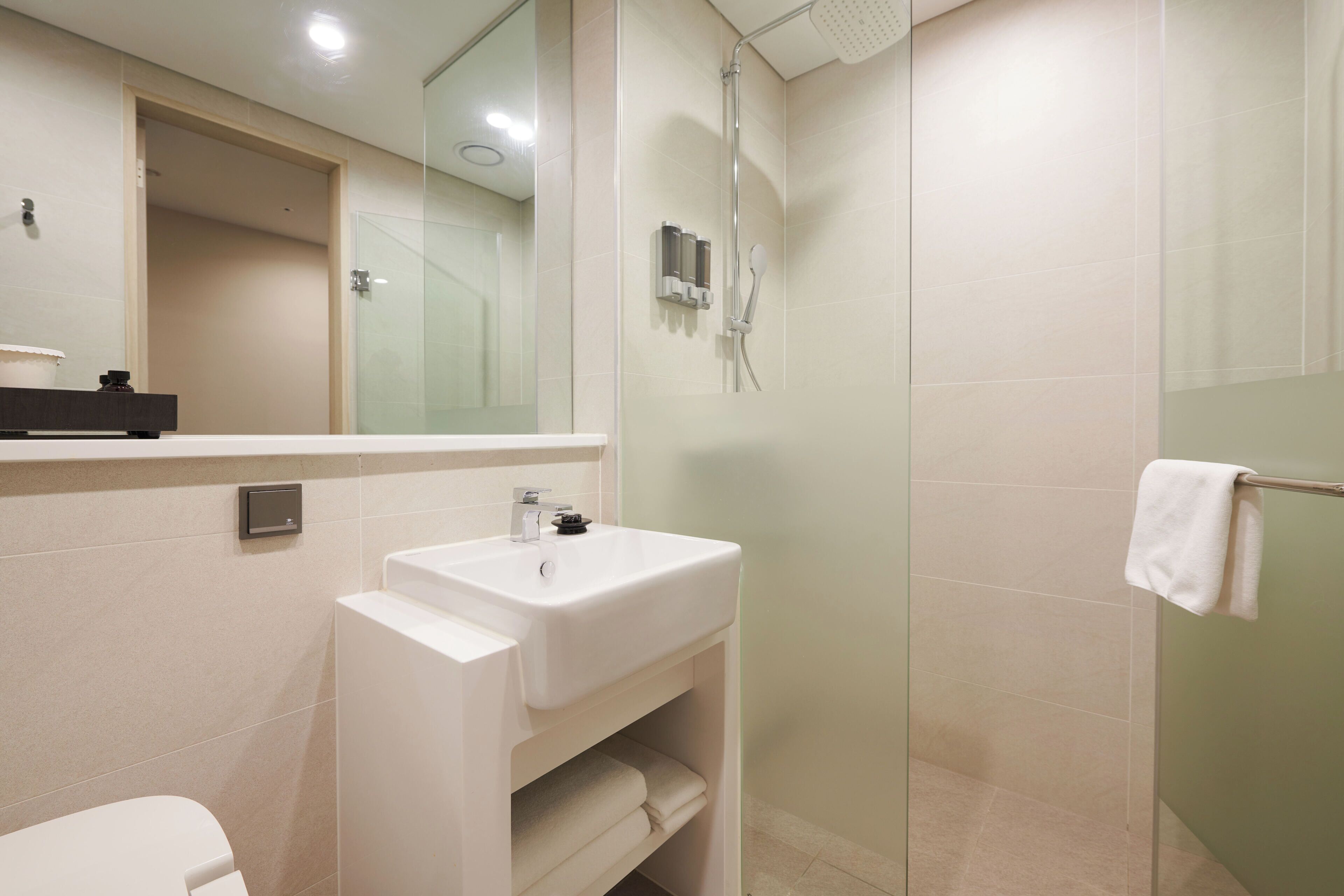 Une salle de bain moderne avec un lavabo blanc, une cabine de douche en verre et une serviette suspendue à un porte-serviettes.