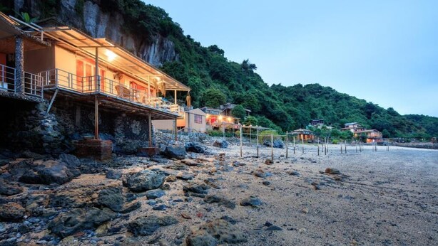Un hôtel situé sur la côte, avec une plage de rochers et une falaise en arrière-plan.
