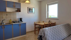 A compact kitchen with blue cabinets, a coffee maker, and a dining table with chairs. - Apartment Adriana 1 for 4 people (Omisalj)