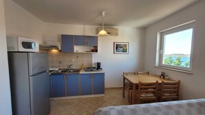 A compact kitchen with a refrigerator, sink, and blue cabinets. There's a dining table with chairs and a window with a view. - Apartment Adriana 1 for 4 people (Omisalj)