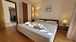 A hotel room with a bed, a bedside table with a lamp, a painting on the wall, and a door leading to another room. - Apartment Adriana 2  for 3 people (Omisalj)