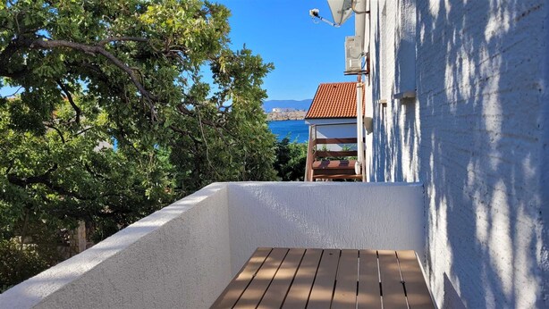 A balcony with a wooden floor, overlooking a body of water and a building with a red roof. - Apartment Adriana 2  for 3 people (Omisalj)