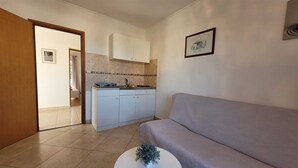 A compact kitchen with white cabinets, a countertop, and a small sink. A grey sofa is positioned in the foreground, and a framed picture hangs on the wall. - Apartment Adriana 2  for 3 people (Omisalj)