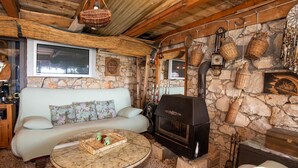 A cozy room with a stone wall, a wooden ceiling, a sofa, a glass coffee table, and a wood-burning stove. - 1 bedroom gorgeous apartment in Komarna (Komarna)