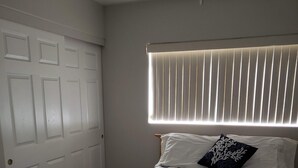 Un dormitorio con una cama, una ventana con persianas y una puerta.