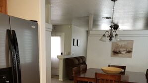 Una cocina con un refrigerador de acero inoxidable, una mesa de comedor con cuatro sillas y un sofá marrón al fondo.