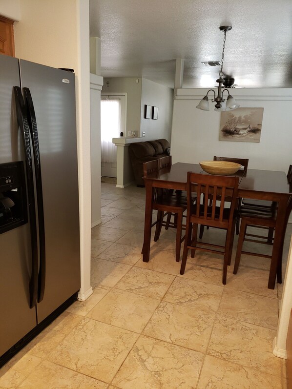 A kitchen with a stainless steel refrigerator, a dining table with four chairs, and a brown sofa in the background.