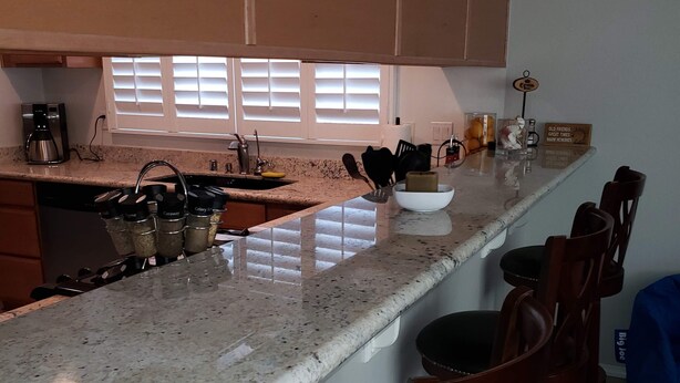 Una cocina con encimera de granito, cafetera y ventana con persianas.