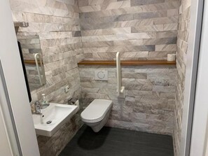 Un baño con pared de piedra, un lavabo blanco y un inodoro.