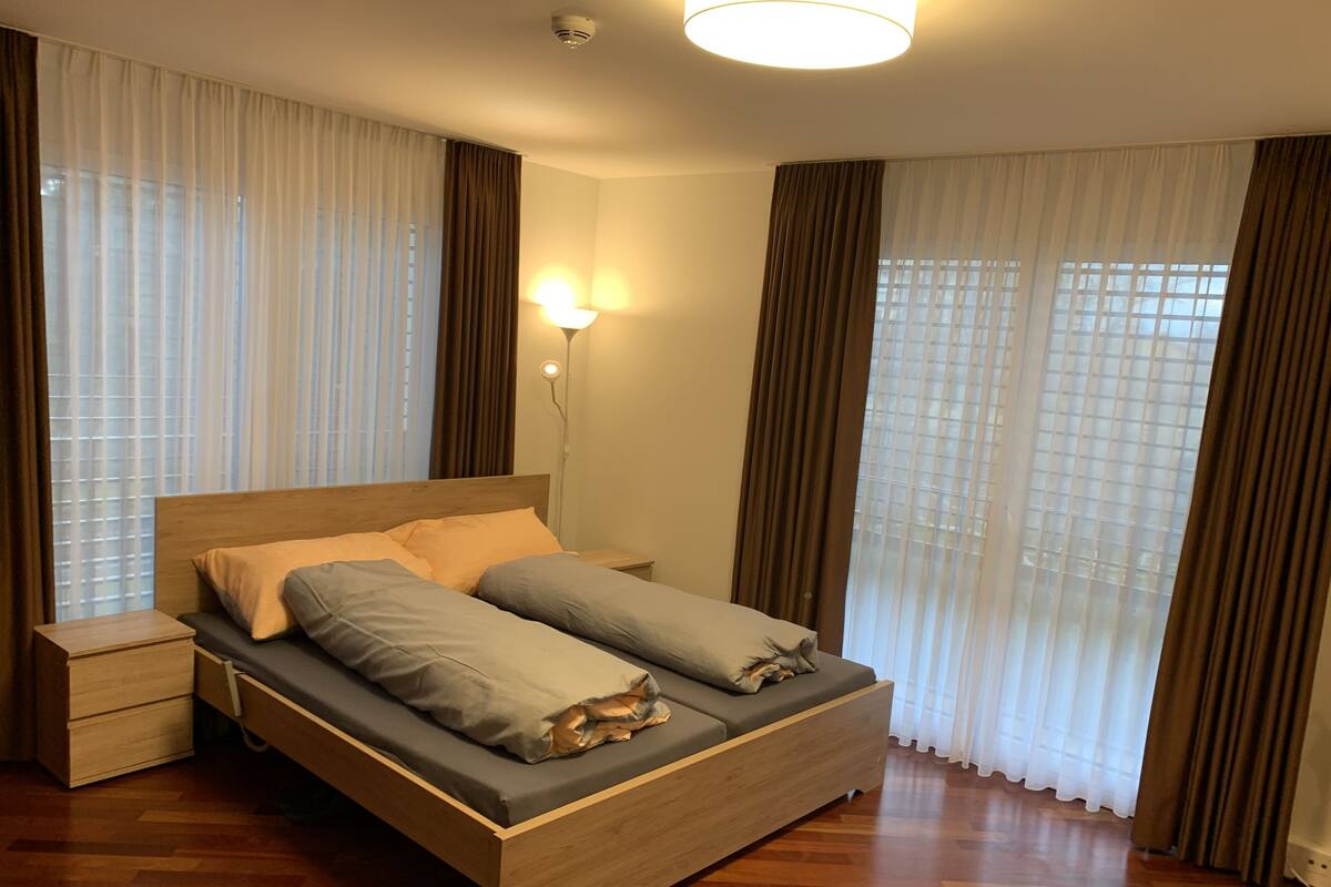 A modern bedroom with a wooden bed, a nightstand, and a wall-mounted lamp.