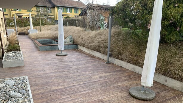 Une terrasse en bois agrémentée de jardinières et d’un petit élément décoratif aquatique.