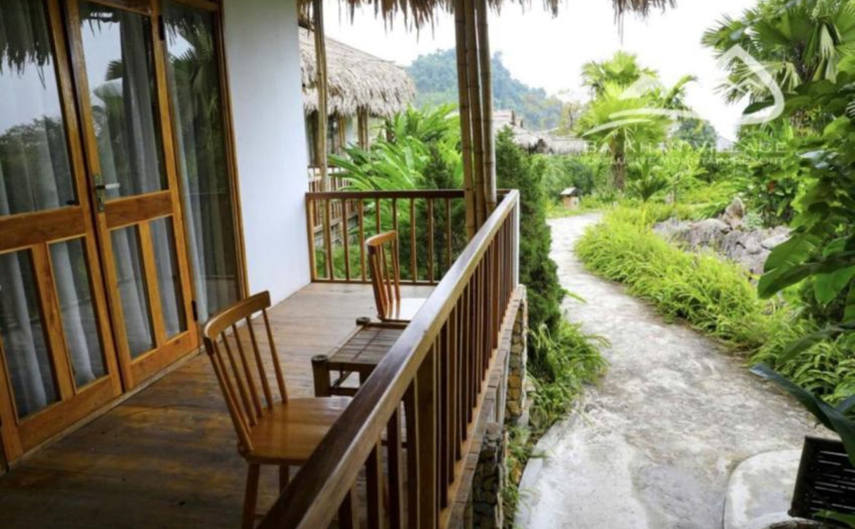 A wooden deck with a bench and a table, overlooking a stone pathway and lush greenery.