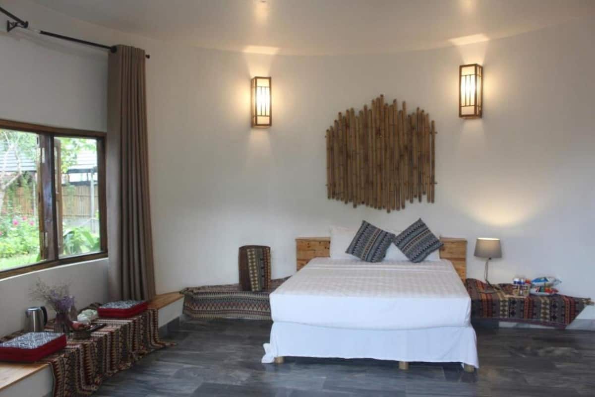 Un dormitorio con una cama grande, dos lámparas de pared, un adorno de bambú en la pared y una ventana con cortinas.