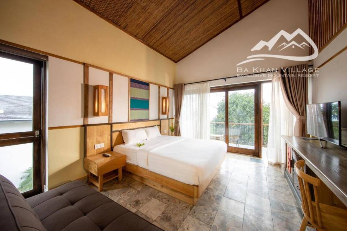 Un dormitorio con una cama grande, cabecera de madera, mesitas de noche, televisor y un balcón con cortinas.