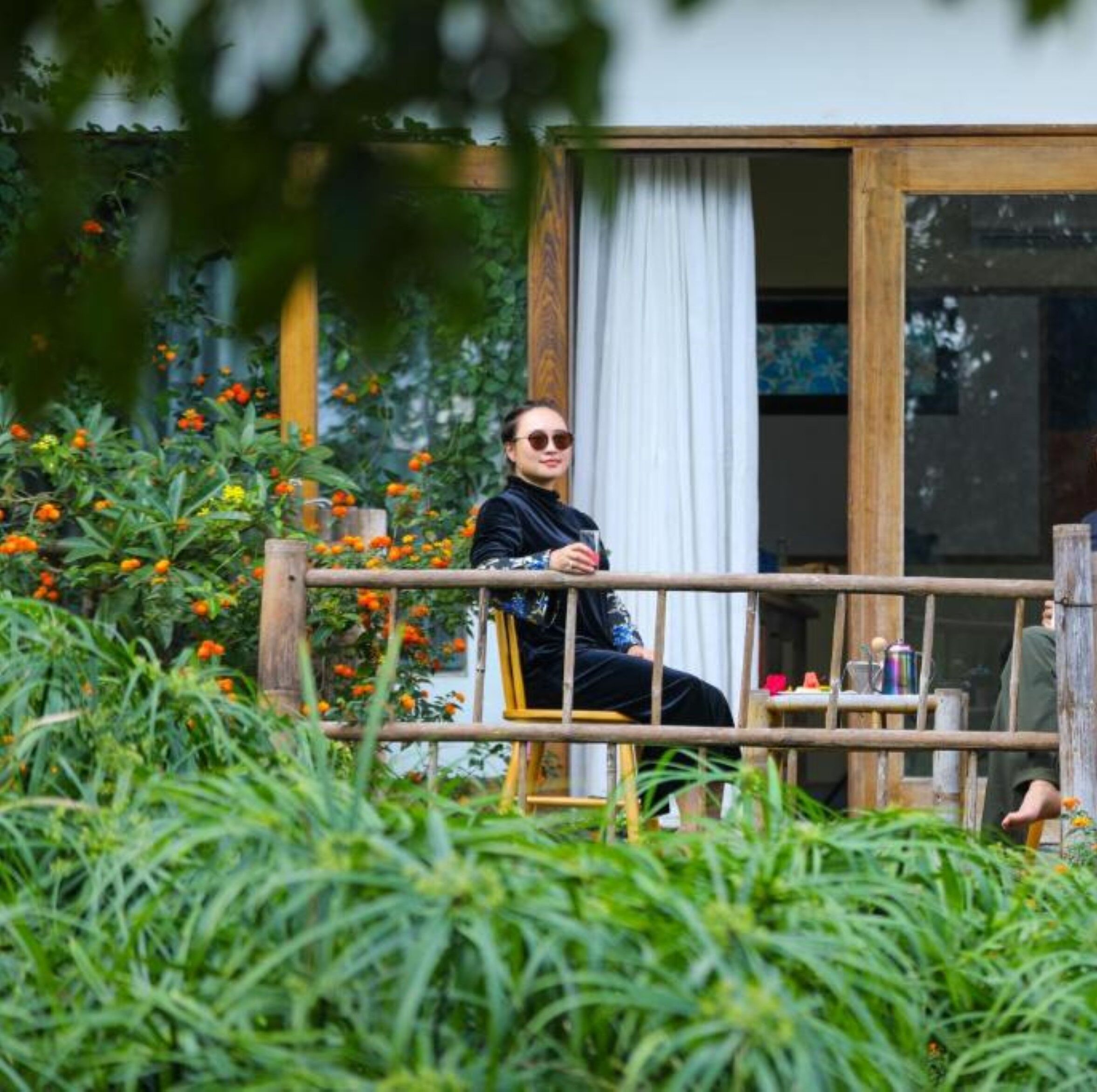 A person sitting on a wooden bench in a garden area with orange flowers and green foliage.