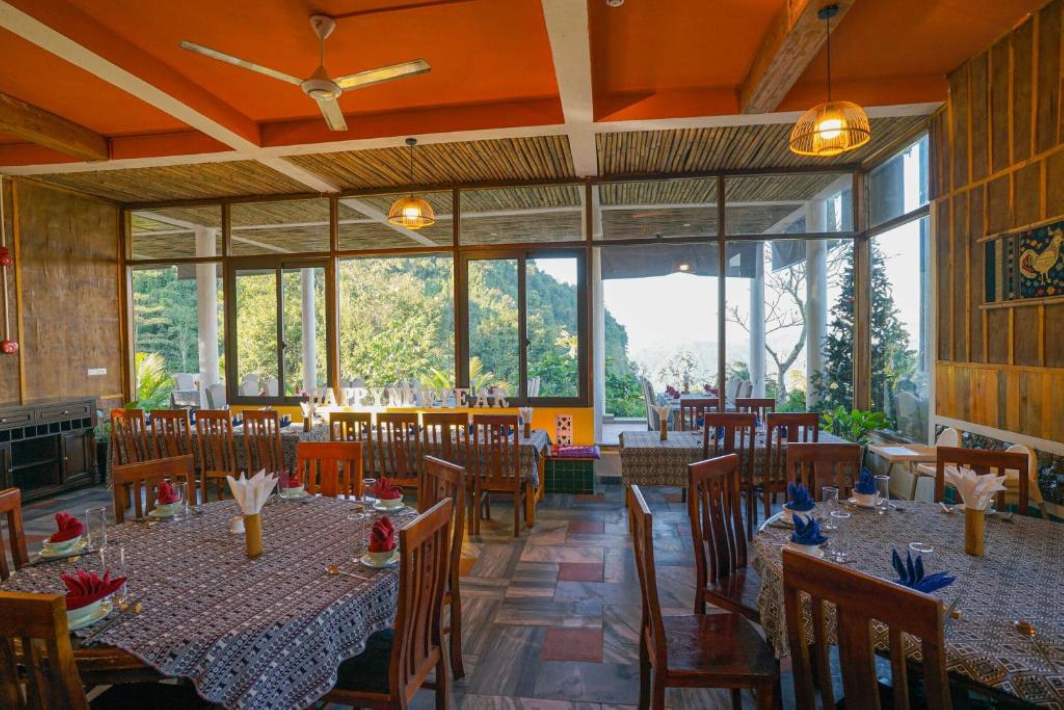 Een restaurant met meerdere tafels, houten stoelen en grote ramen met uitzicht op het buitenland.