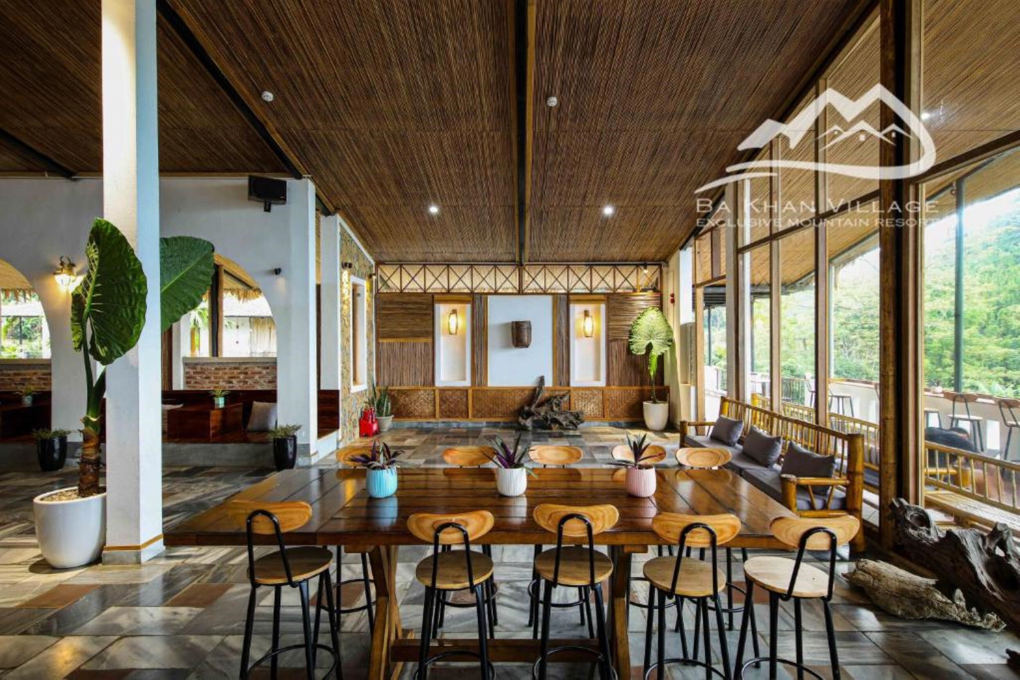 Un comedor amplio con una larga mesa de madera y sillas, rodeado de ventanas grandes que ofrecen vistas al exterior.