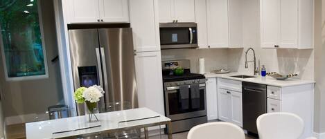 A modern kitchen with white cabinets, stainless steel appliances, and a dining area with a glass table and white chairs.