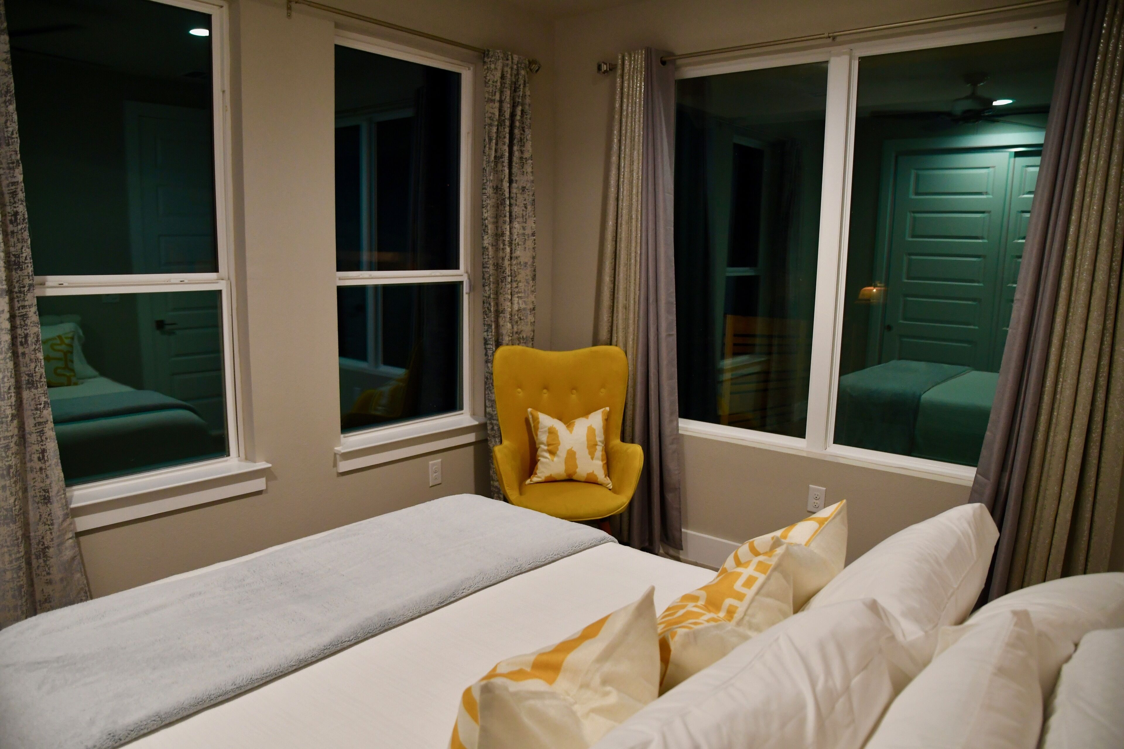 Una habitación de hotel con una cama, un sillón amarillo y dos ventanas.