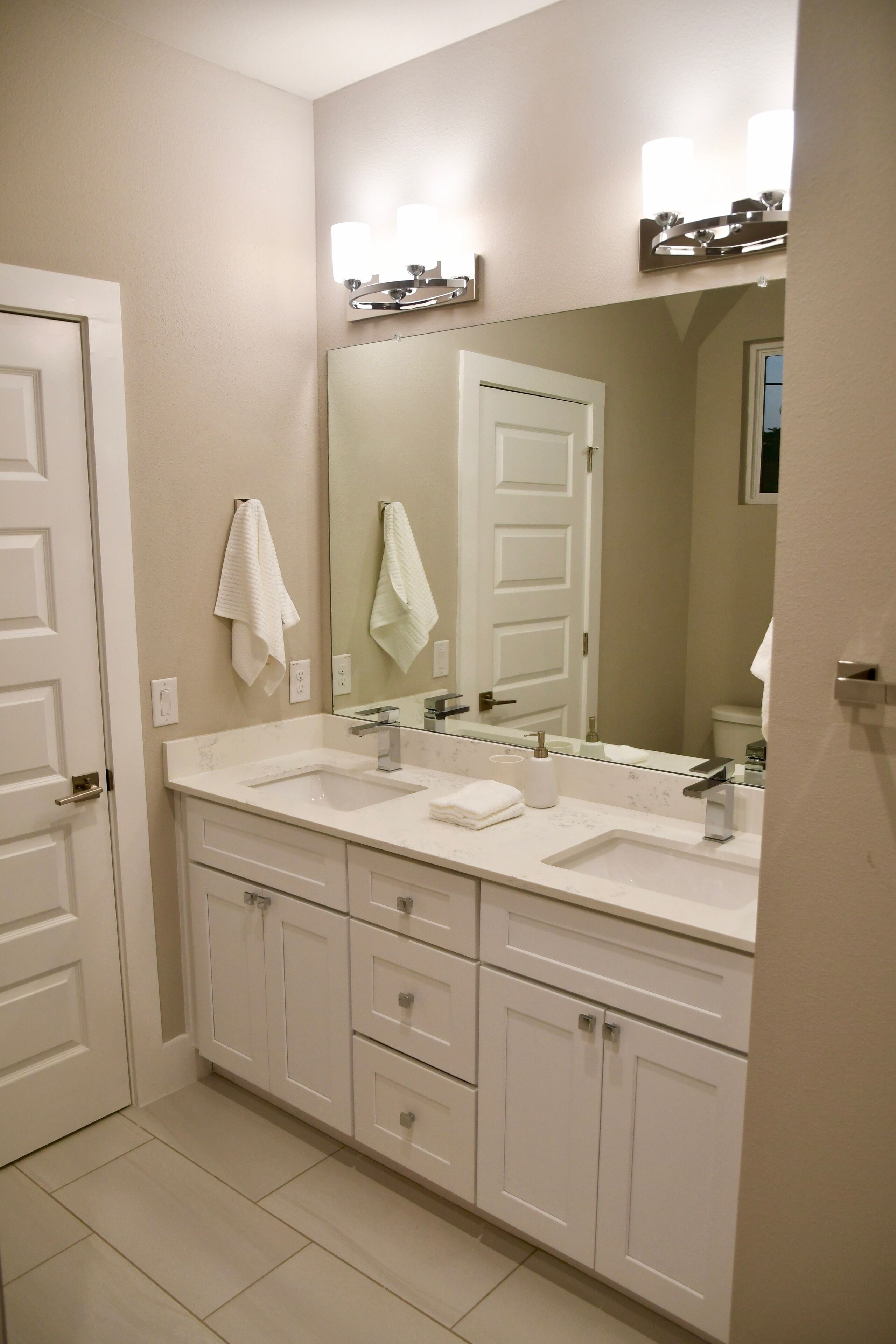 Une salle de bain avec deux lavabos, un grand miroir et des meubles blancs.