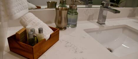 A bathroom with a marble sink, a wooden tray holding toiletries, and a mirror reflecting a vase with flowers.