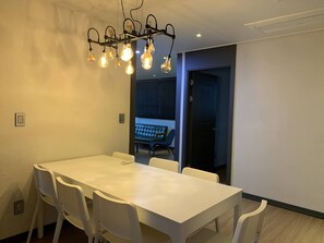 A dining area with a long white table, white chairs, and a modern light fixture.