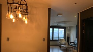 A modern dining area with a white table and chairs, a hanging light fixture, and a large window offering a view of the city.