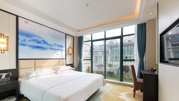 A hotel room with a large bed, a desk, a chair, a TV, and a painting on the wall. - Yiwu Luck Bear Hotel (Jinhua)
