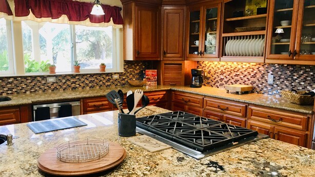 A kitchen with granite countertops, wooden cabinets, a gas stove, and a window with curtains. - Central Coast Casa II (Atascadero)