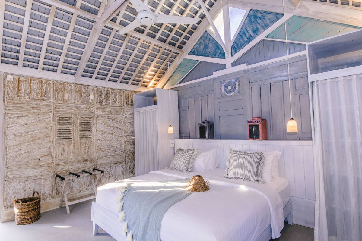 Een slaapkamer met een groot bed, een houten hoofdbord, een plafondventilator en een raam met uitzicht.