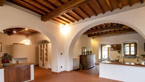 A spacious kitchen with a herringbone floor pattern, wooden beams on the ceiling, and a central island with a sink and countertop.