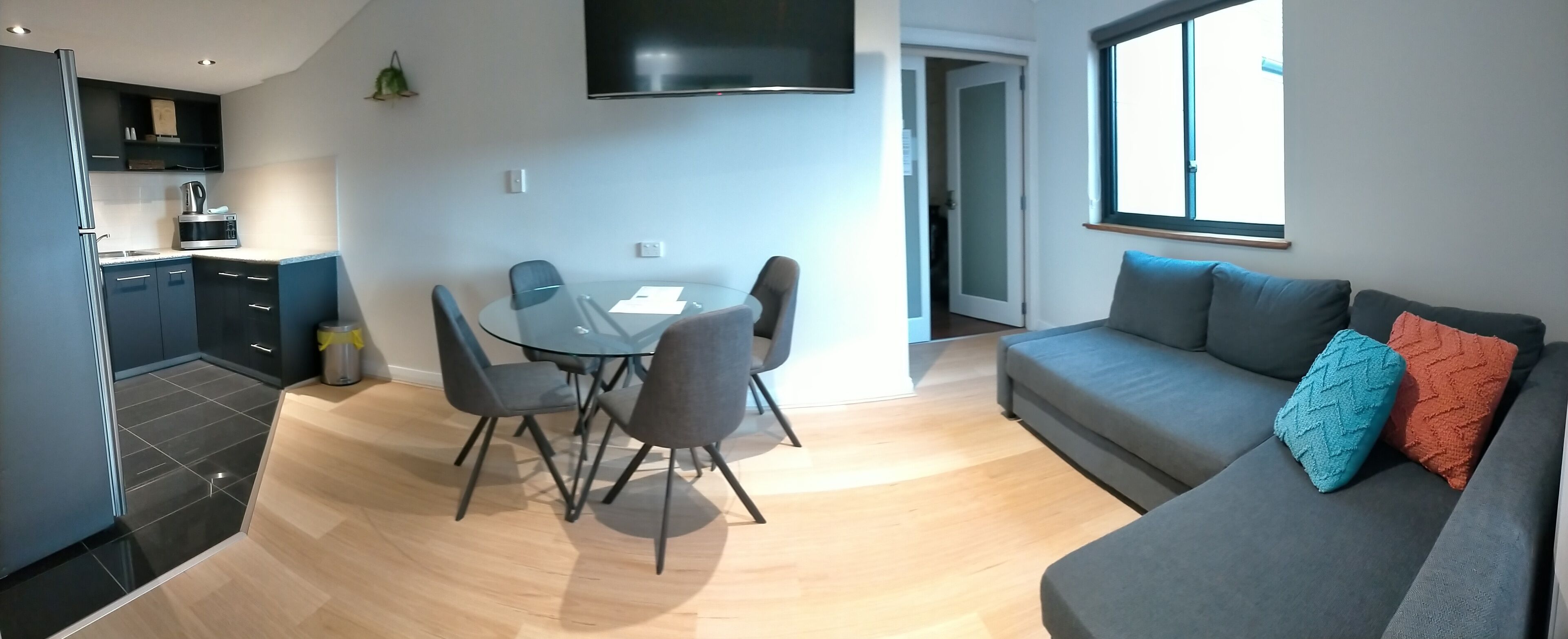 A modern living space with a dining area, a sofa with cushions, and a kitchen.