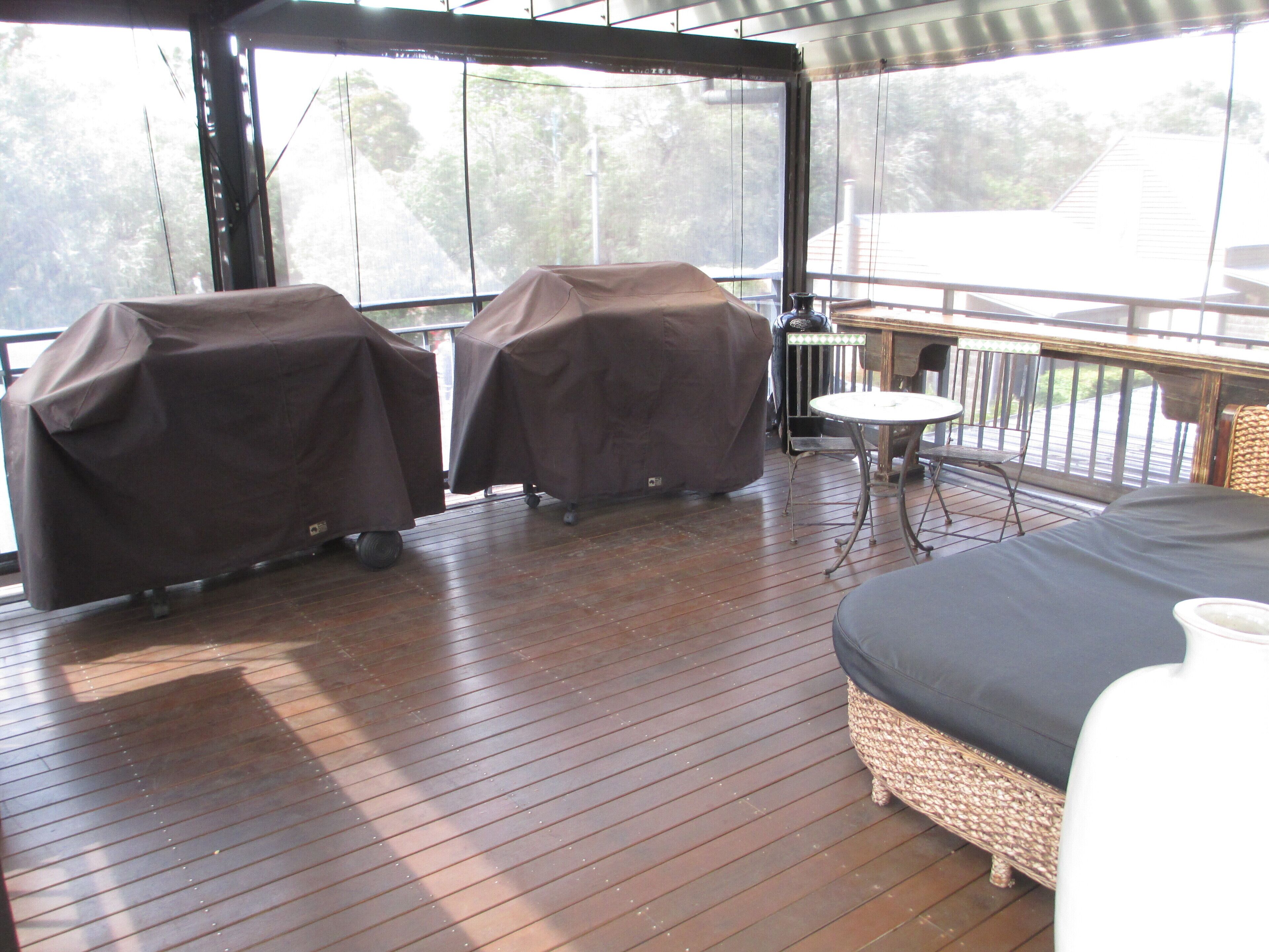 An outdoor deck with two barbecue grills covered in brown cloth, a round table, and a wicker sofa.