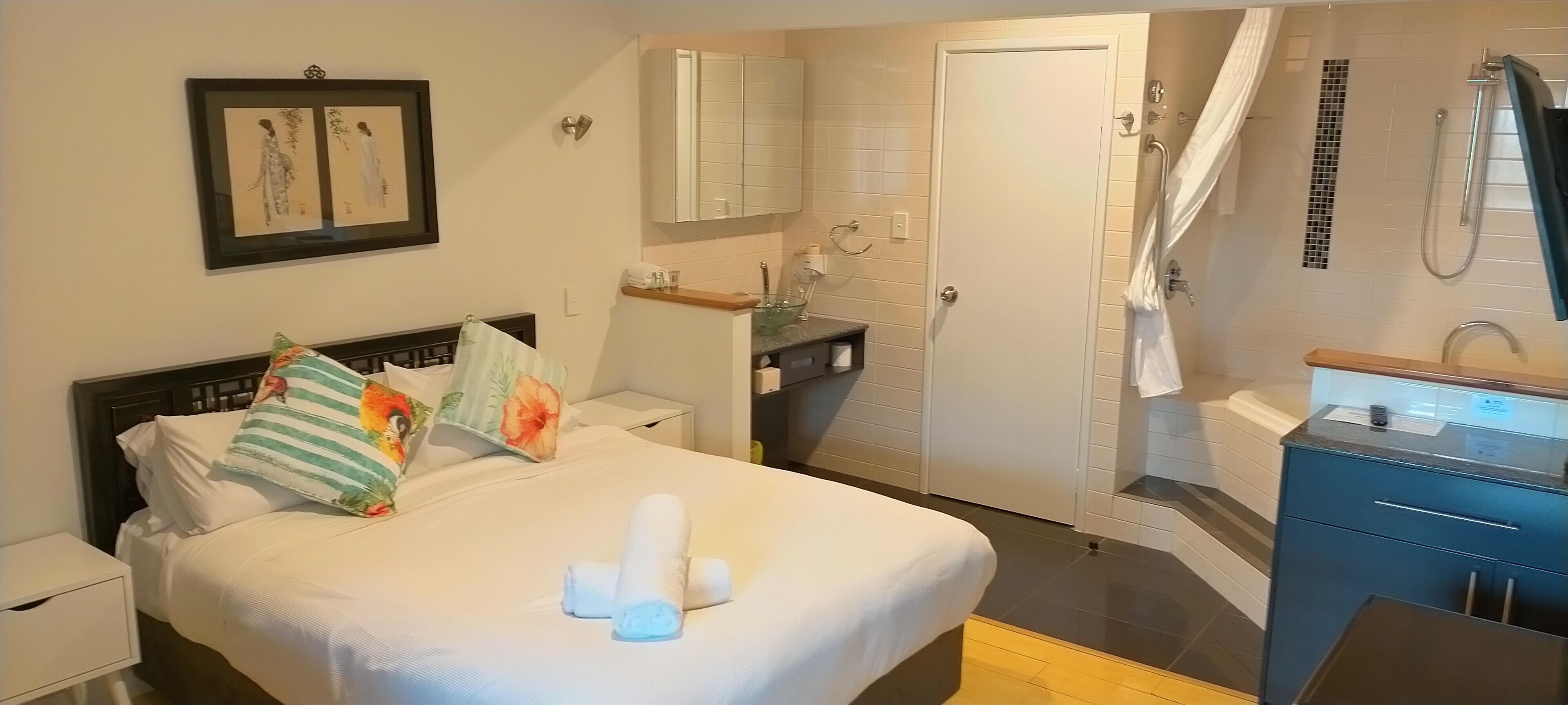 A hotel room with a bed, a nightstand, a bathroom with a shower, and a small desk with a chair.