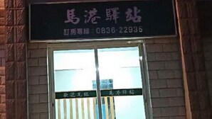 Letrero con caracteres chinos y un número de teléfono sobre una puerta de cristal con una verja de metal.
