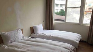Una habitación con dos camas, una ventana con cortinas y vistas a edificios.