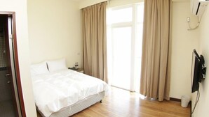 Una habitación de hotel con cama, mesita de noche, televisor y ventana con cortinas.
