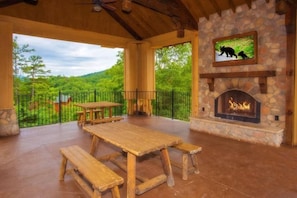 A covered patio with a stone fireplace, wooden benches, and a table. - Stunning View | Hot Tub & Resort Pool Access (Sevierville)
