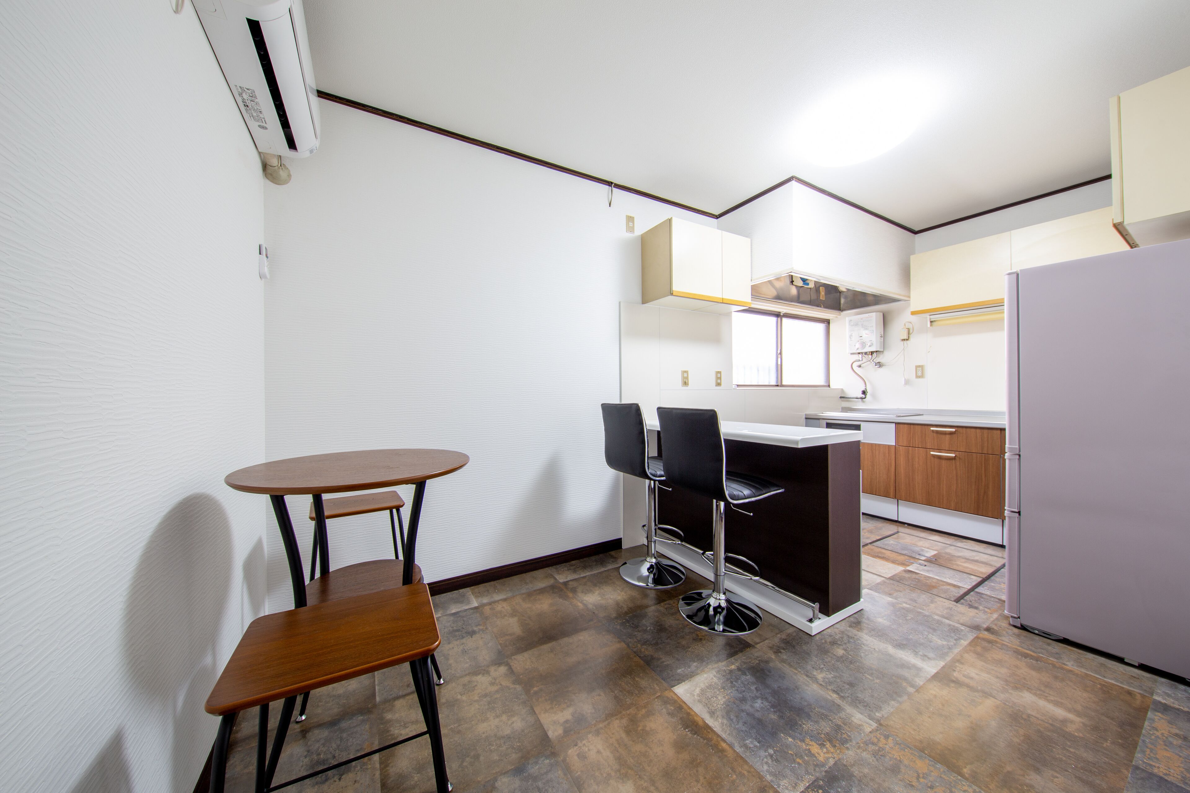 A compact kitchen with a dining area, featuring a small table and two chairs, a refrigerator, and wooden cabinets.