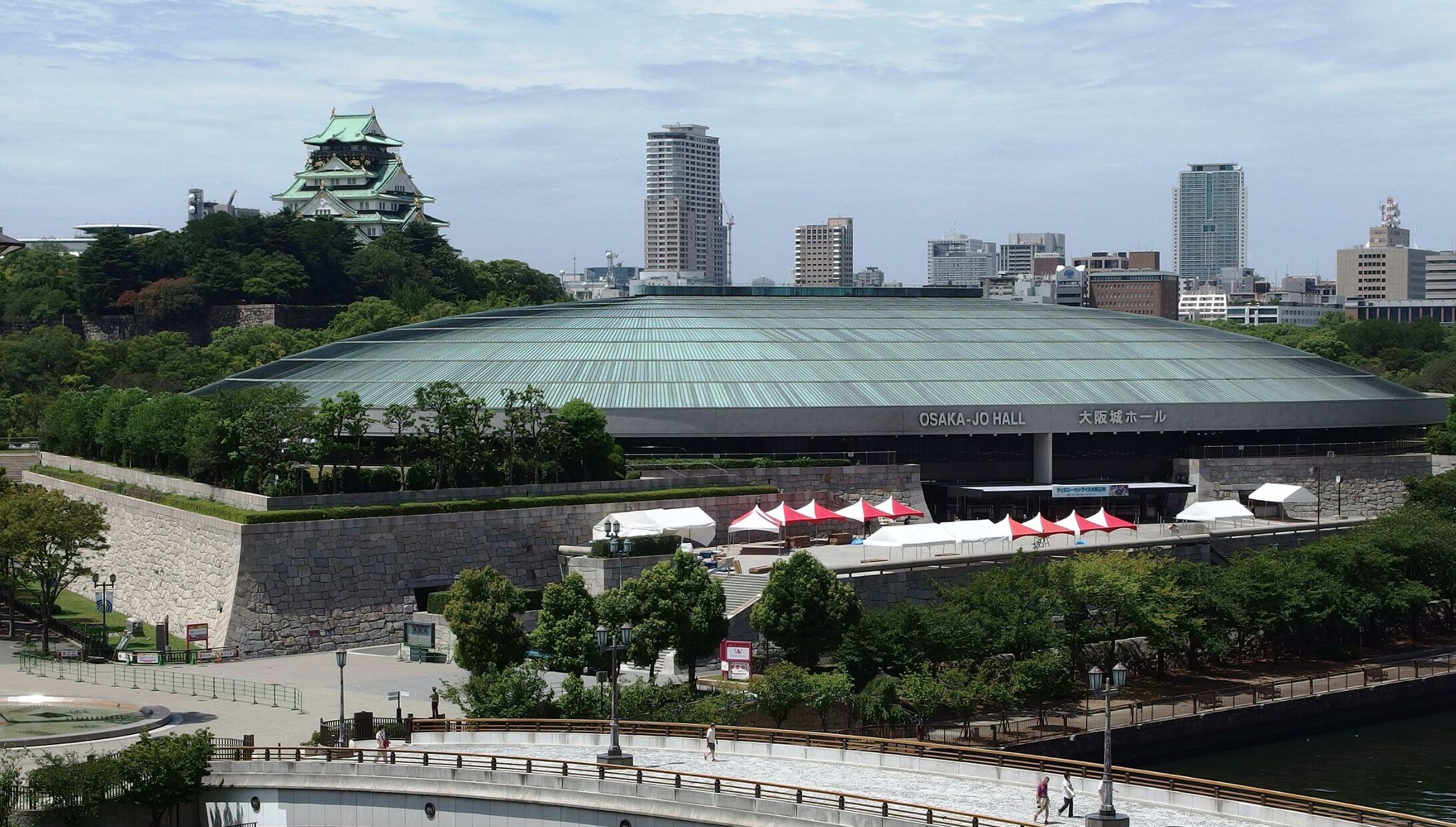 A large stadium with a green roof, surrounded by trees and a river.