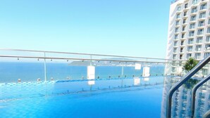 A pool with clear blue water, a metal railing, and a view of the ocean and a building in the background. - Sunkiss Hotel (Nha Trang)