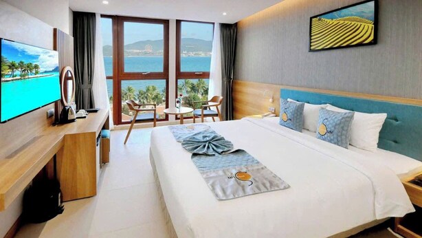 A hotel room with a bed, a TV, a desk, and a view of the sea. - Sunkiss Hotel (Nha Trang)