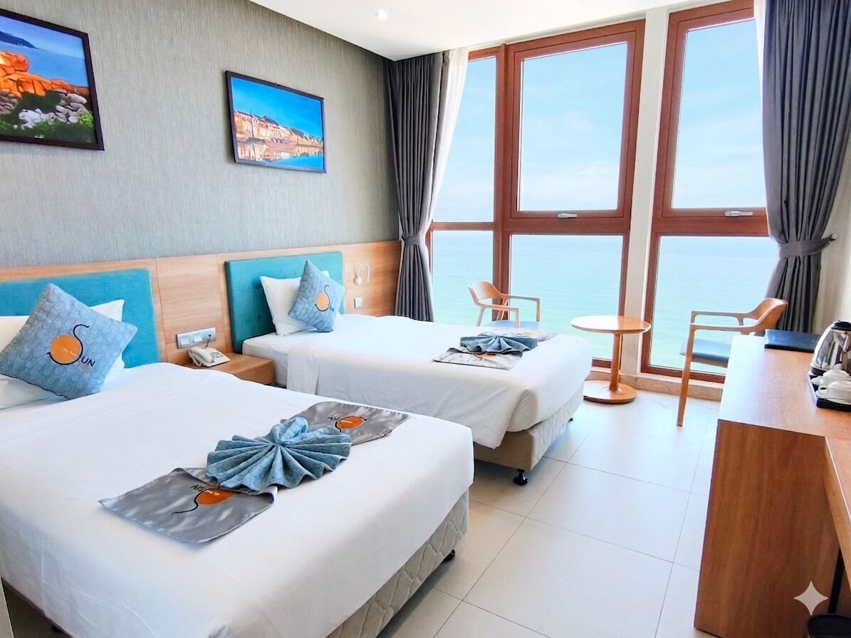 Camera d'albergo con due letti, un tavolino, una sedia e vista sul mare.