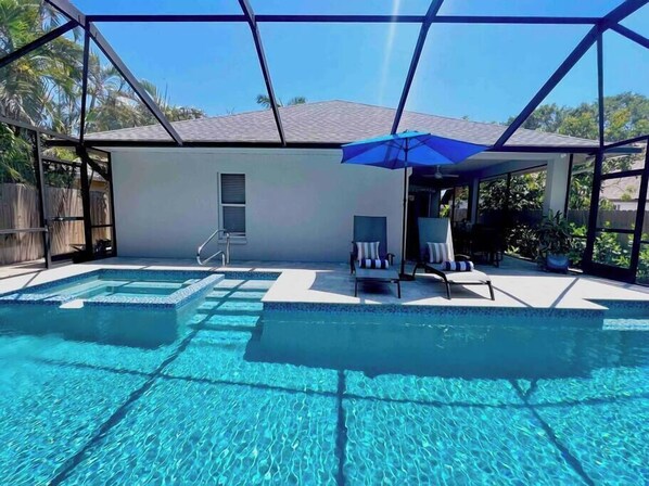 A swimming pool with clear water, a covered patio area, and lounge chairs.