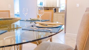 A dining area with a glass table, chairs, and a kitchen in the background. - 555 Royal Palm Villa | Luxury Heated Pool Home (Naples)