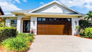 A residential house with a garage, brick driveway, and landscaped garden. - 555 Royal Palm Villa | Luxury Heated Pool Home (Naples)