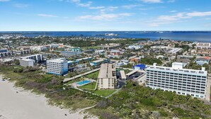 Luchtbeeld van een kustplaats met een mix van commerciële en woongebouwen, een strand en een uitgestrekte waterpartij in de verte.