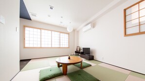 Ein Zimmer mit Tatami-Matten, einem Tatami-Tisch, einem Fernseher und einer Schiebetür.