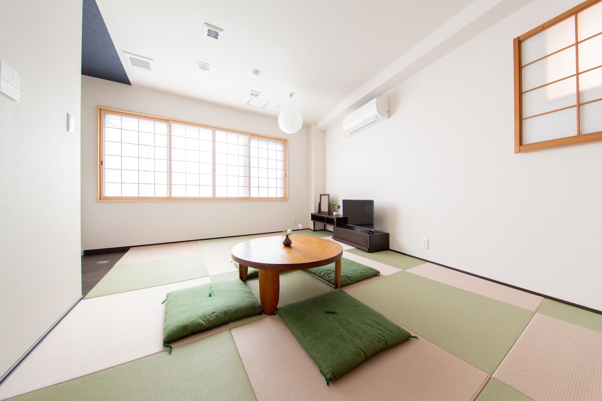 Une pièce avec des tatamis, une table en tatami, un téléviseur et une porte coulissante.