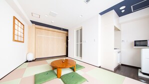 Ein Zimmer mit Tatami-Matten, einem Tatami-Tisch, einem Futon-Bett, einer Schiebetür und einer Mikrowelle.